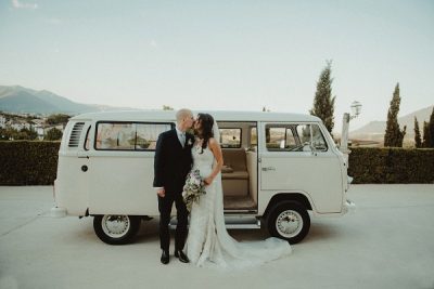 Beautiful white wedding campervan with a newly married couple kissing in front of it. 