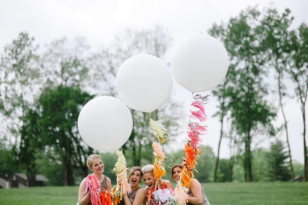 Bride and bridesmaids holding giant white balloons with bright pink and orange tassels.