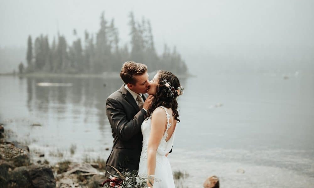 Newly weds kissing by a beautiful misty lake.