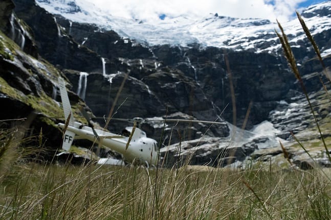 White helicopter lands in a mountainous valley surrounded by green grass.