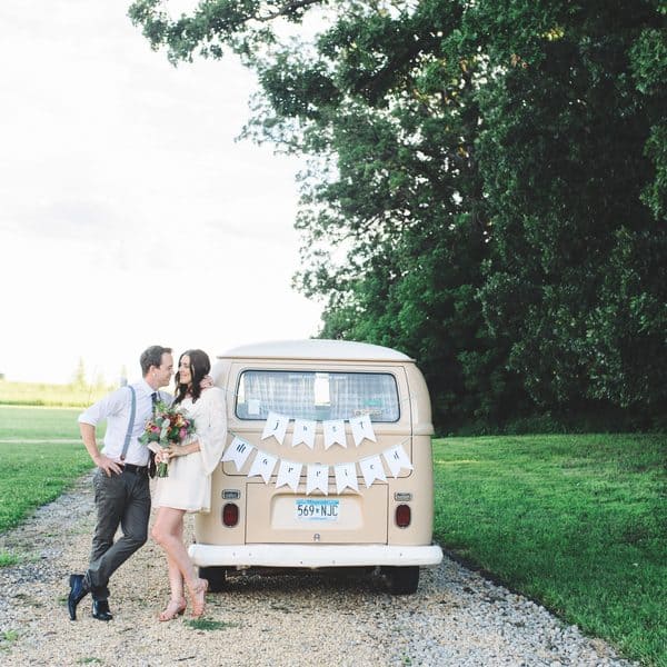 Couple kissing outside a beige campervan decorated with just married bunting.