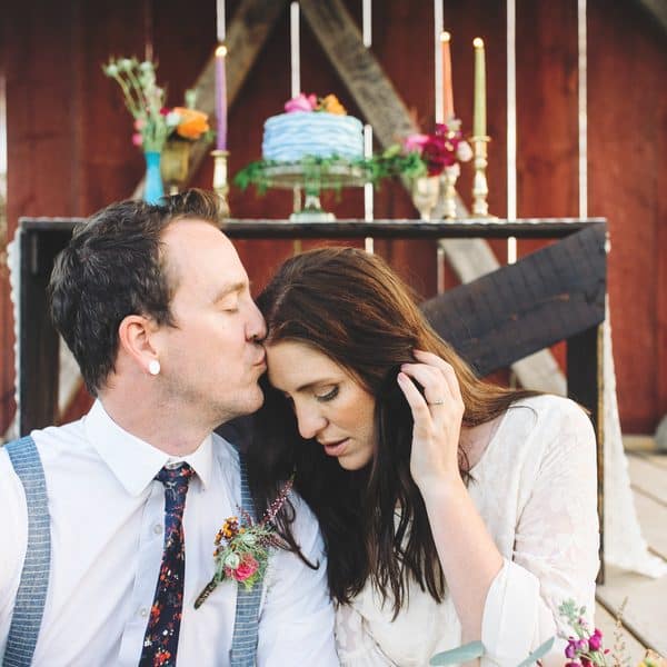 Man kisses woman on the head while sitting in a barn.