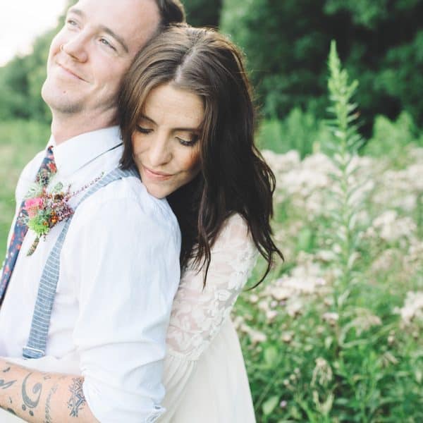 Woman hugs man from behind in a rural setting.