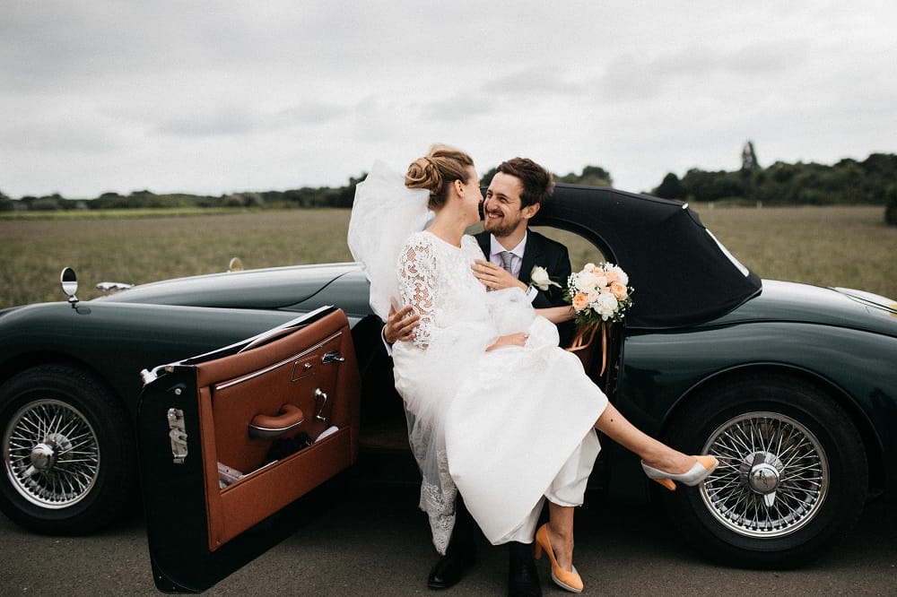 Bride sits on the grooms lap in their wedding car.